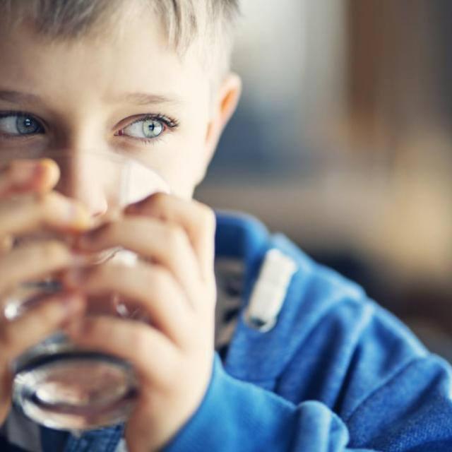Enfant en pull bleu buvant un verre d'eau
